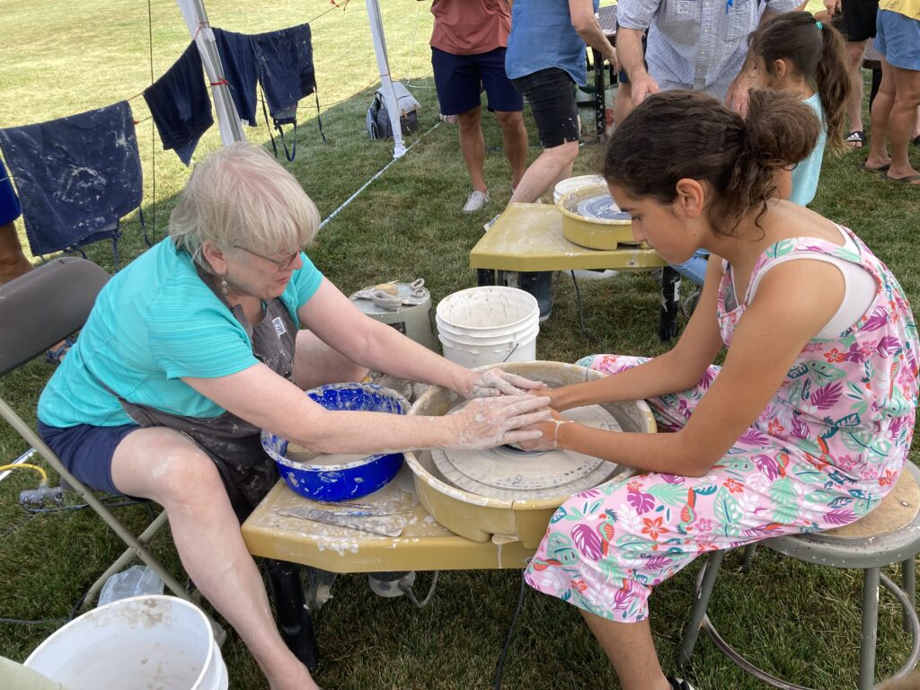 Artist helping a gril throw pottery at Family Art Day